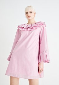 Ροζ φόρεμα με ρυτιδωμένο λαιμό και φουσκωτά μανίκια. Φτιαγμένο από ελαφρύ ύφασμα, με διακριτή υφή και σχέδιο μέχρι το γόνατο.