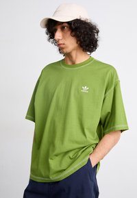 T-shirt en coton vert oversize avec des coutures blanches contrastantes et un petit logo Adidas blanc sur la poitrine gauche.