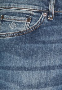 Jeans de denim con un clásico lavado azul, diseño de cinco bolsillos, costuras en contraste y un pequeño parche de la marca en el bolsillo frontal.
