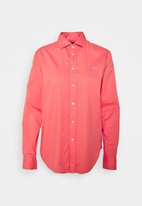 Korallfärgad skjorta med knappar i bomull; har en klassisk krage, långa ärmar och en liten blå logotyp på vänster bröst.