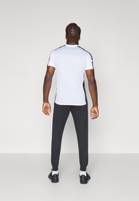 White short-sleeve shirt with black side accents, paired with dark gray joggers. The outfit features a casual fit and smooth texture.