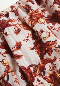 Tissu à motifs floraux en crème avec des fleurs vibrantes orange et jaunes. Texture lisse avec des sections froncées et un fond à rayures subtiles.