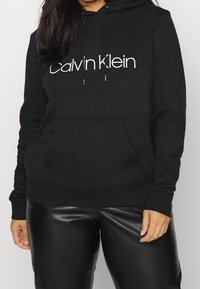 Felpa nera in cotone con logo bianco "Calvin Klein", tasca a marsupio frontale, cordini regolabili e polsini e orlo a costine.
