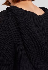 Felpa nera lavorata a maglia con un design texturizzato e spesso e un ampio scollo. Presenta un cappuccio che scende lungo la schiena.