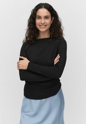 Haut noir texturé à manches longues avec un décolleté bateau, associé à une jupe en satin bleu clair. Le haut présente un détail de taille froncée.