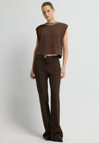 Hnědý krátký top s límcem zdobeným perlami, spárovaný s hnědými úzkými kalhotami s předním zlatým knoflíkem. Hladká textura, uvolněný střih.