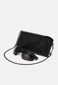 Black leather handbag with a geometric design, paired with dark sunglasses featuring a textured frame and gradient lenses.