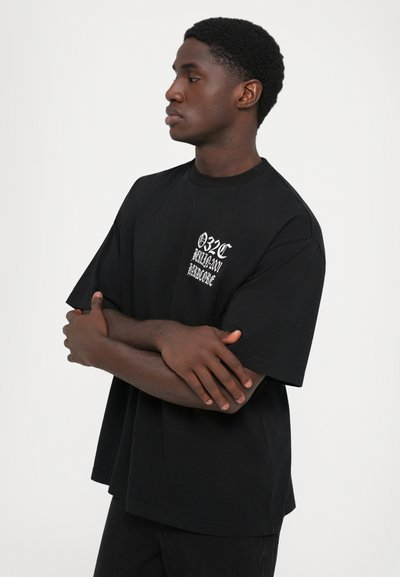 T-shirt noir à manches courtes avec col rond et coupe ample, présentant un texte graphique blanc sur le côté gauche de la poitrine. Matière en coton doux.