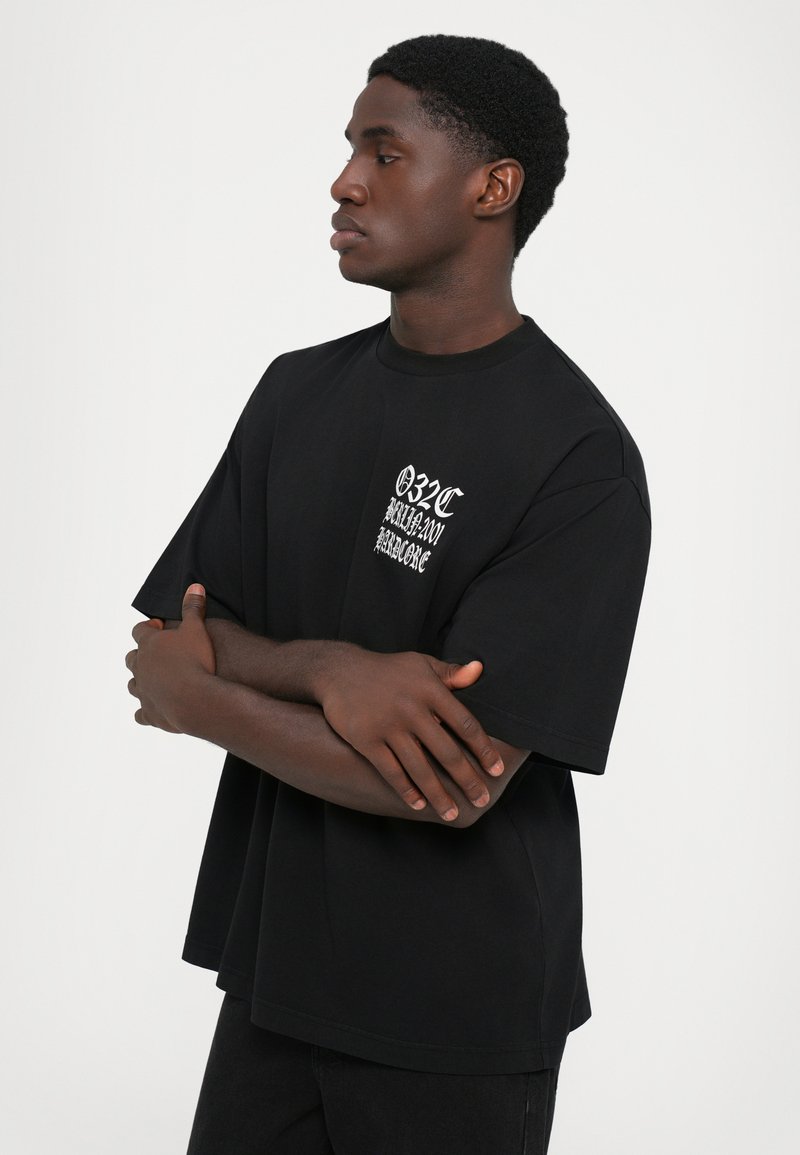 Black short-sleeve t-shirt with a crew neck and loose fit, featuring white graphic text on the left chest area. Soft cotton material.