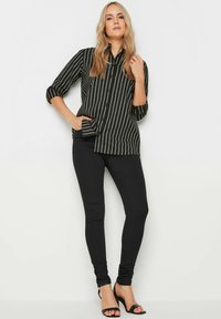 Camicetta a righe bianco e nero con maniche arrotolate, abbinata a jeans skinny neri e sandali con tacco alti neri.