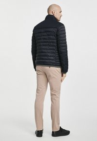 Niebieska kurtka puchowa z poziomym pikowaniem i wysokim kołnierzem. W zestawie z jasnobeżowymi chino i czarnymi sneakersami.