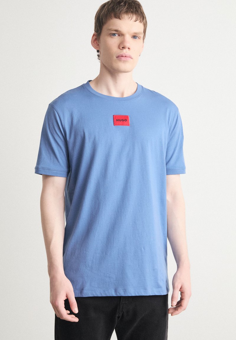 Svijetloplavi pamučni t-shirt s kratkim rukavima, okruglim izrezom i crvenim pravokutnim oznakom s tekstom "HUGO" na prsima.