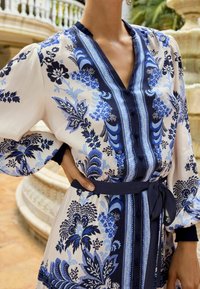Vestito con motivo floreale in avorio e blu navy, caratterizzato da scollo a V, patta con bottoni e cintura coordinata. Tessuto morbido con maniche a palloncino.