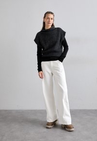 Haut gris foncé en maille avec un col montant, superposé à un chemisier noir à manches longues, associé à un pantalon blanc à jambes larges et des bottines à plateforme marron.