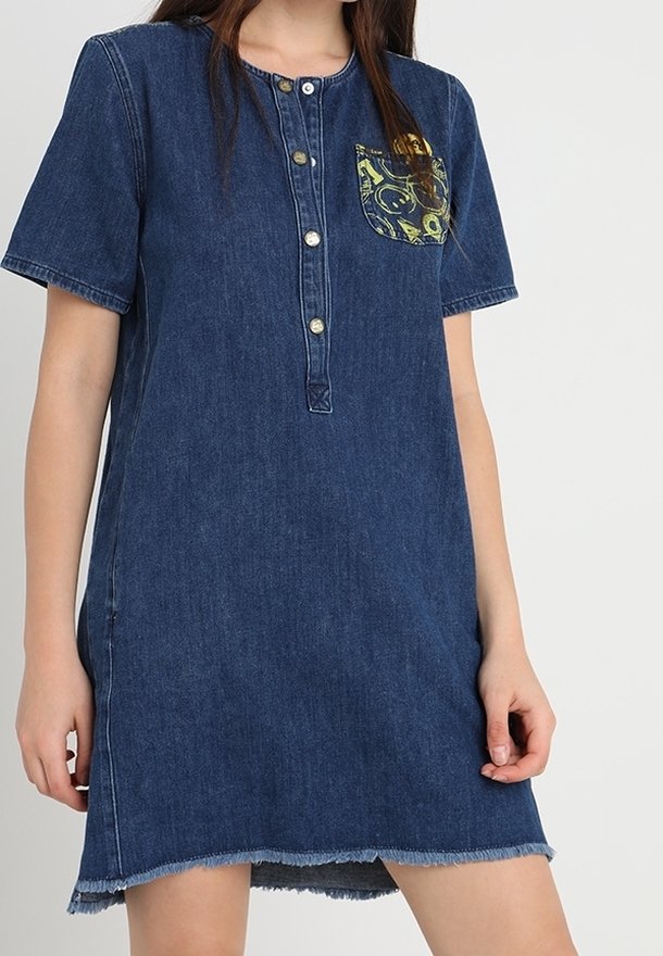 Denim-paitamekko lyhyillä hihoilla, napitettuna edestä ja taskulla, jossa on värikäs kuvio. Repaleinen helma tuo lisäyksityiskohtia.