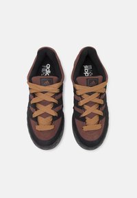 Hnědé a černé sportovní boty s textilním svrškem, texturovanou gumovou podrážkou a světle hnědými tkaničkami. Tři černé pruhy na stranách.