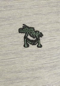 Grün gestickter Hund auf einem beige-weißen gestreiften Stoffhintergrund, Nahaufnahme des strukturierten Strickmaterials.