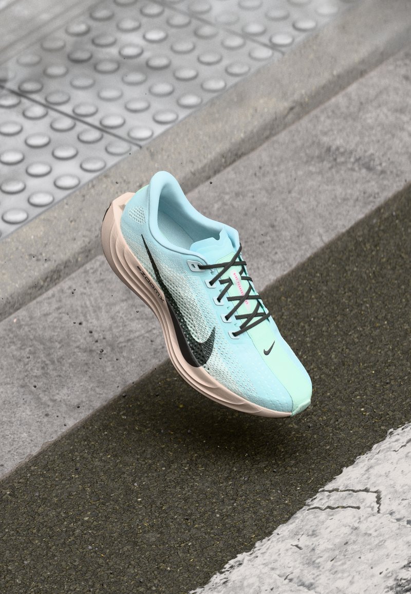 Chaussure de course Nike avec une tige en mesh bleu clair, des accents noirs et des détails roses. Équipée d'une semelle rembourrée beige et de lacets noirs.