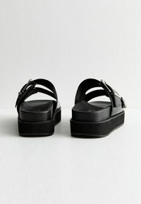 Sandali platform neri con una finitura in pelle liscia, fasce incrociate e dettagli metallici, dotati di una soletta imbottita e un tacco leggero.