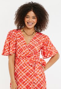 Rotes karierte Wickelkleid mit kurzen Puffärmeln, das einen Gürtel in der Taille hat und kontrastierende Muster aus Karos und Punkten in verschiedenen Rottönen zeigt.