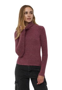Maglione a collo alto a coste di un profondo colore mauve, realizzato in tessuto testurizzato. Caratterizzato da maniche lunghe e un design aderente, abbinato a pantaloni scuri.