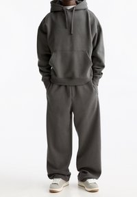 Grå huvtröja med frontficka, matchande grå sweatpants och beige sneakers, med en avslappnad passform och mjukt, texturerat tyg.