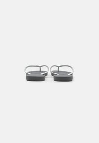 Chinelos cinzentos com tiras finas e palmilha texturizada, apresentando um design minimalista e uma sola plana. Sem hardware ou acentos notáveis.
