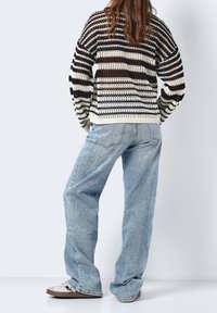 Gestrickter Pullover mit schwarz-cremefarbenem Streifenmuster, lockere Passform; kombiniert mit hellblauen Jeans und beigen Turnschuhen.