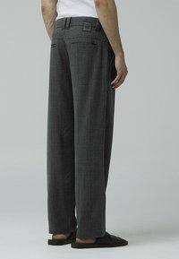 Gray checked trousers with a loose fit, featuring back pockets and a textured fabric. Worn with a white tank top and black slip-on shoes.