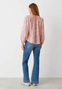 Blusa a maniche lunghe con un motivo a spirale rosa e rosso, in tessuto leggero e dal taglio morbido, abbinata a jeans blu svasati.