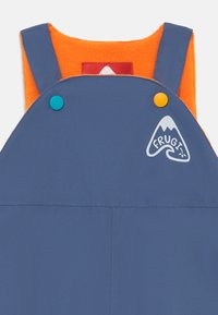 Blaue wasserdichte Latzhose mit orangefarbenem Fleecefutter, verstellbaren Trägern und zweifarbigen Knöpfen. Mit dem FRUGI-Logo in Weiß.