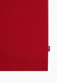 Tissu en coton rouge avec des coutures visibles sur le bord inférieur et une petite étiquette rouge de la marque Levi's sur le côté droit.