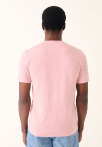 Pink bomuld T-shirt med korte ærmer, en rund halsudskæring og en glat overflade, vist bagfra mod en neutral baggrund.
