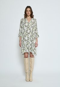 Blumengemustertes Kleid aus leichtem Stoff, mit V-Ausschnitt, 3/4-Ärmeln und rüschengesäumtem Saum, kombiniert mit kniehohen beigen Stiefeln.