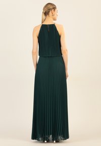Grünes, plissiertes Halterkleid mit taillierter Blende und fließendem Rock. Verfügt über ein Schlüssel-Loch am Rücken und metallische Akzente an den Schultern.
