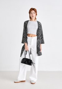 Zwart-wit gemusterd kimono, grijze crop top, witte wide-leg broek, met een kleine zwarte handtas, grijze sneakers en een schone achtergrond.