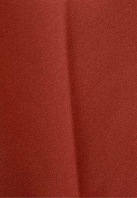 Gros plan d’un tissu texturé de couleur orange rouille avec un pli doux courant verticalement près du centre.