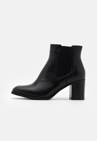 Stivale alla caviglia in pelle nera con pannello elastico rigato sui lati, punta affusolata e tacco spesso con un'accortezza metallica sul retro.