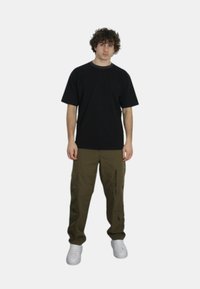 T-shirt nera in cotone a maniche corte, abbinata a pantaloni cargo verde oliva con zip e tasche, completata da sneaker bianche.