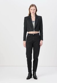 Korte zwarte blazer met reliëfstructuur, gedragen over een denim top. Zwarte high-waisted jeans met een taps toelopende pasvorm en enkellaarsjes.