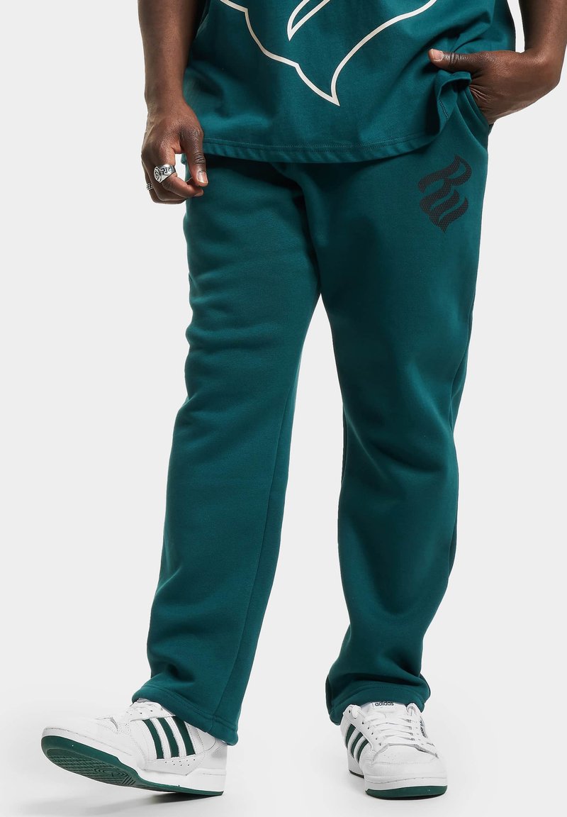 Teal joggingbroek met een ontspannen pasvorm en een zwart logo detail. Gecombineerd met witte sneakers met groene accenten en drie stroken.