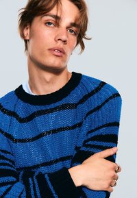 Maglione lavorato a maglia di colore blu con strisce nere, caratterizzato da un collo a giro e un motivo testurizzato. Include polsini e orlo a coste.