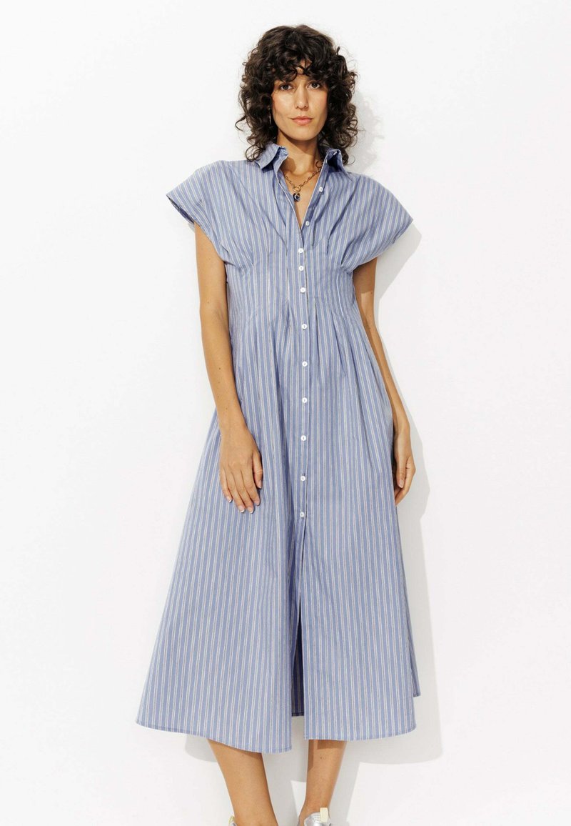 Robe chemise rayée bleue en tissu léger avec des manches courtes à empiècement et une jupe évasée à mi-genoux. Présente un col et des boutons.