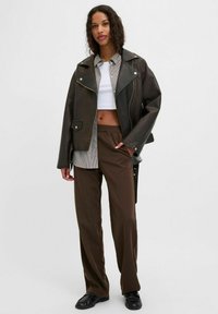 Brogas ādas jaka ar sudraba elementiem, saskaņota ar baltu īsu topu un svītrainu pogājamu krekla, kā arī brīvām brūnām biksēm. Melni apavi.