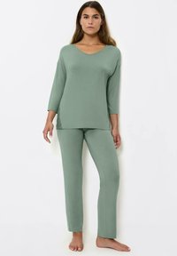 Conjunto de loungewear verde claro que incluye una camiseta de cuello en V con mangas tres cuartos y pantalones a juego. Tejido suave con una textura lisa.