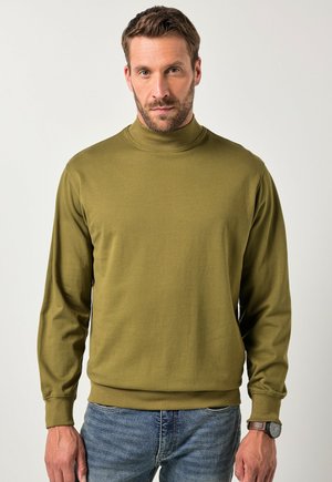 Suéter de cuello alto en verde oliva con mangas largas, puños y dobladillo acanalados. Hecho de material suave, con una textura lisa. Llevado con jeans.