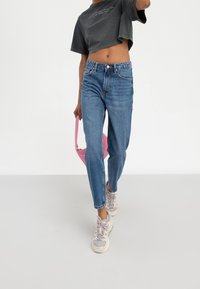Højtaljede blå jeans med lige snit, parret med en cropped grå t-shirt. Looket afsluttes med beige og grå sneakers samt en pink taske.
