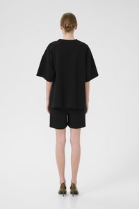 Čierne oversized tričko s ramenami s poklesom, spárované so zodpovedajúcimi čiernymi šortkami. Oblečenie je vyrobené z mäkkej tkaniny a má voľný strih.