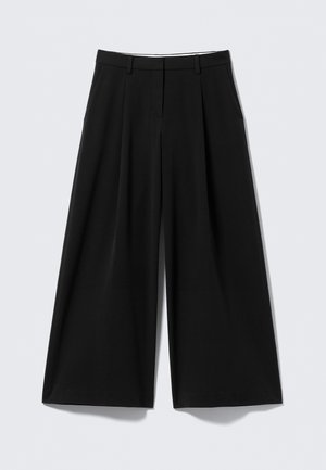 Mustad laiad püksid ees volditega, küljetaskud, vöökohaga ja peidetud esikinnitusega valgel taustal.