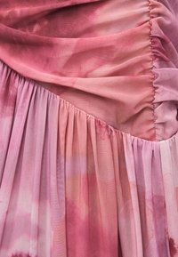 Tissu tie-dye rose et violet avec des parties rassemblées et plissées, montrant une texture douce, transparente et des plis superposés.